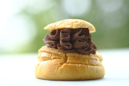 Sweet eclair lies on a wooden tray. Delicious dessert. Spring greens on the background.