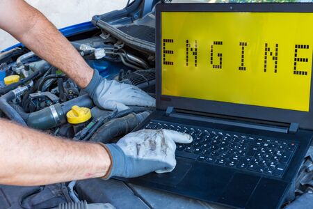 mechanic working on the engine of a car with a computerの写真素材