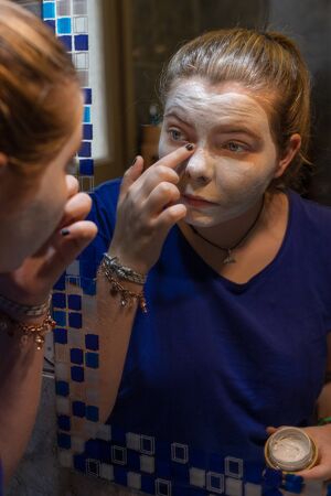 young girl putting cream on her face in front of the mirror