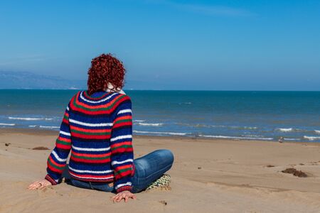 woman sitting on the sand looking at the sea in winter with a sweaterの写真素材