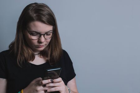 young blonde girl with glasses interacting with a smartphone, on a gray background