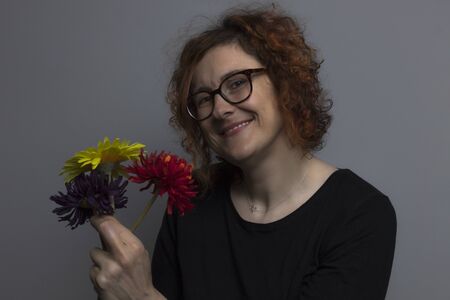 smiling redhead woman with three red, yellow and purple flowers in her handの写真素材
