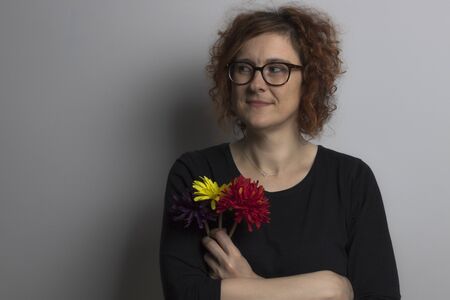 smiling redhead woman with three red, yellow and purple flowers in her handの写真素材