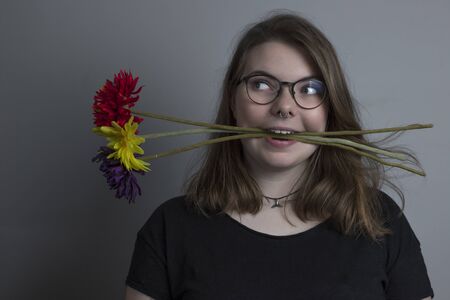 young blonde girl with three red, yellow and purple flowers in her mouthの写真素材