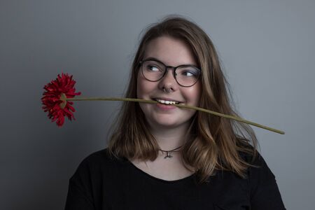 young blonde girl with a red flower in her mouthの写真素材