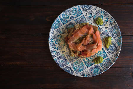salmon tartar with avocado, fresh tomato, tuna, anchovies and olive oil in a blue plate on a wooden tableの写真素材