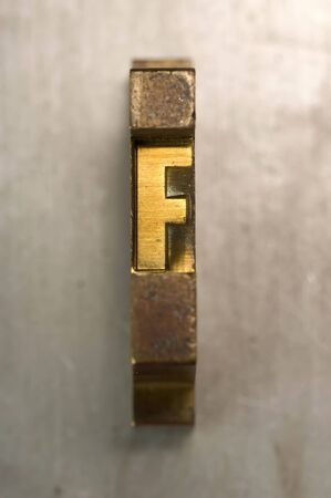 Brass / Gold colored letterpress piece on silver metal backgroundの写真素材