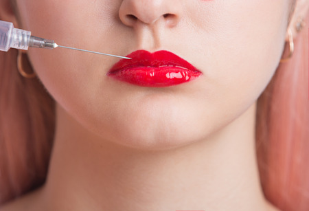 Beautiful young woman is getting an injection in her lips. close upの写真素材