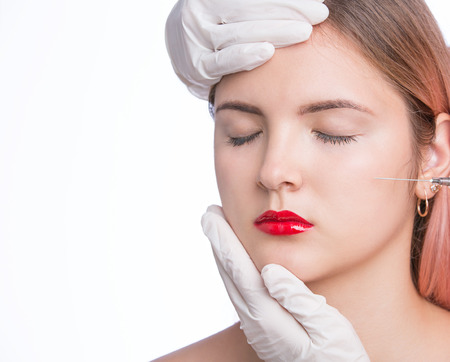 Beautiful young woman gets beauty injection in cheek. Isolated on whiteの写真素材