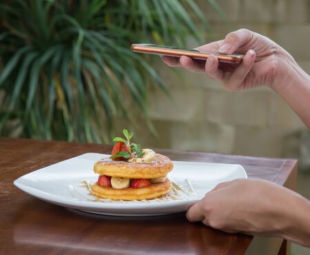 Pancake with banana and strawberry. Young girl takes picture with her phone