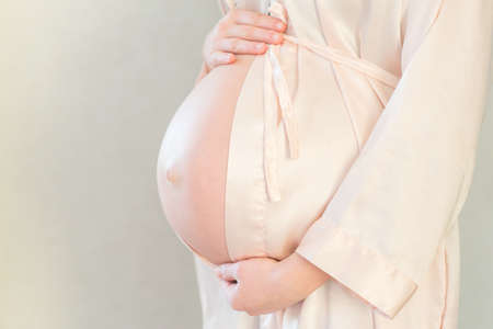 Unrecognizable pregnant woman with hands over tummy at grey backgroundの写真素材
