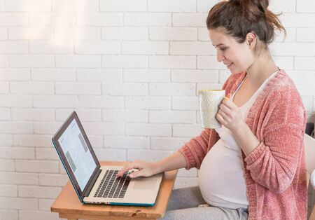 Pregnant woman working online on the laptop at homeの写真素材