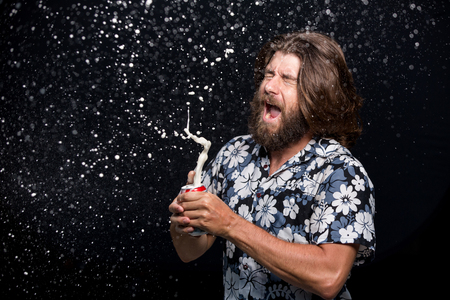 Man opens a bottle of cold beer spraying with splashes on black background