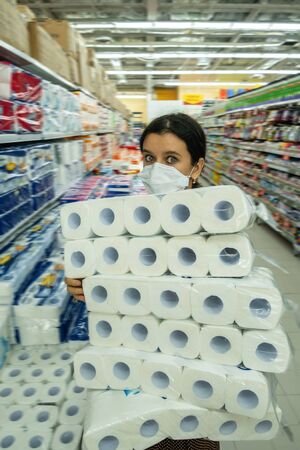 Alarmed female wears medical mask against coronavirus while buying tissues or toilet papersの写真素材