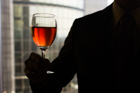 Silhouette of businessman holding a glass of wine in hotel.の写真素材