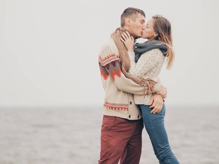Young attractive couple in knitted sweaters on a cliff on sea shore, kissing, creative toningの写真素材