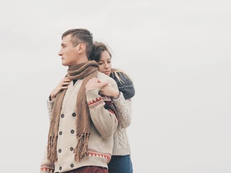 Young attractive couple in knitted sweaters on a cliff on sea shore, hugging and holding hands, creative toningの写真素材