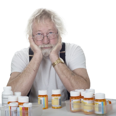 senior wearing glasses with a lot of prescription bottles of pills isolated on whiteの写真素材