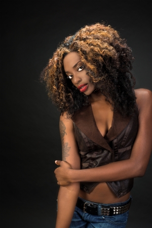 Beautiful African American woman with gorgeous lips wearing jeans and a vest against a dark backgroundの写真素材