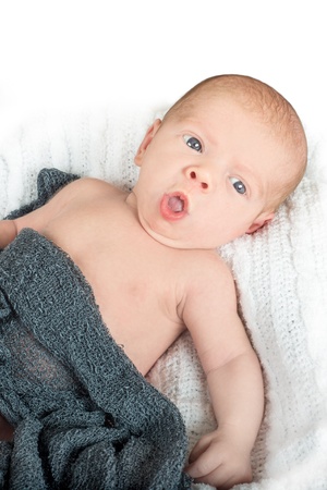 Awake baby with surprised look on his face and blue eyes lying on a white blanketの写真素材