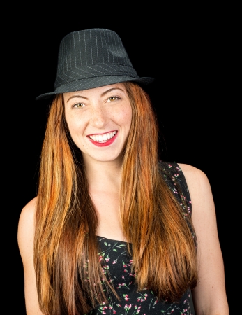 Happy smiling young woman with long red hair and hazel eyes wearing a pinstriped fedora isoaled on blackの写真素材