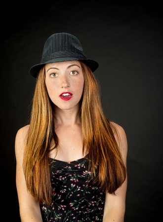 Very cute girl with red hair freckles and beautiful hazel eyes wearing a pinstriped fedora against a dark backgroundの写真素材