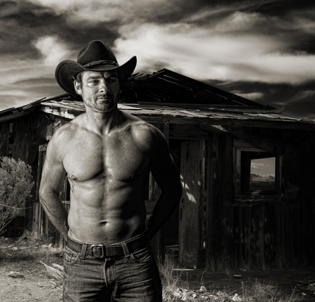 Cowboy at dusk in front of an old cabin in monochrome toned sepiaの写真素材