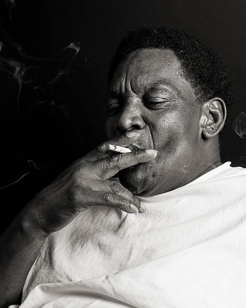 Serious African American Man smoking a cigarette against a dark backgroundの写真素材