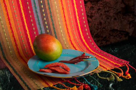 Chili lime mango slices with dried chilis and fresh mango on a rustic blue plate and colorful  Mexican Print placematの写真素材