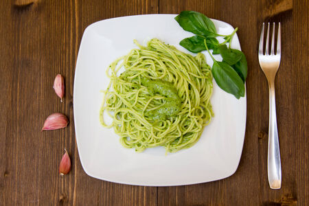 Spaghetti with pesto on wooden table with fork and garlic 