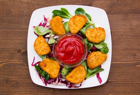 Nuggets of chicken over salad on wooden table seen from aboveの写真素材