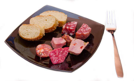 Pieces of salami and bread slices on plate on white background