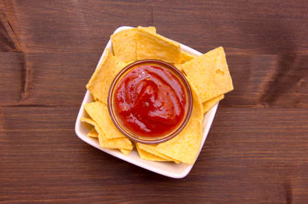 Bowl with corn chips and hot sauce on wooden table top view