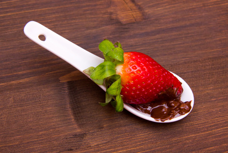 Teaspoon with strawberry and chocolate on wooden table seen from aboveの写真素材