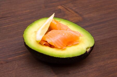 Half an avocado with smoked salmon on wooden tableの写真素材
