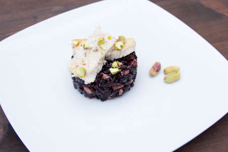 Black rice with fish and pistachios on a wooden table seen up closeの写真素材