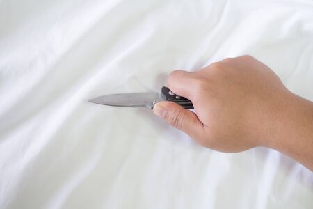Man hand hold the folding knife on the white bed