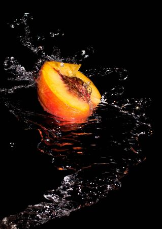 Half a peach in a spray of clean transparent water on a black backgroundの写真素材
