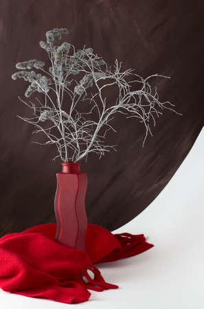 Silver bouquet of dried plants in a vase with curly red scarf at the bottom, still lifeの写真素材