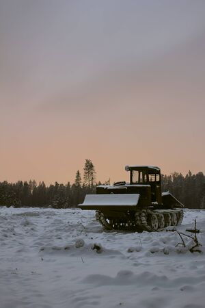 Tractor for removal of trees covered with snow on the background of carved forest in the twilightの写真素材