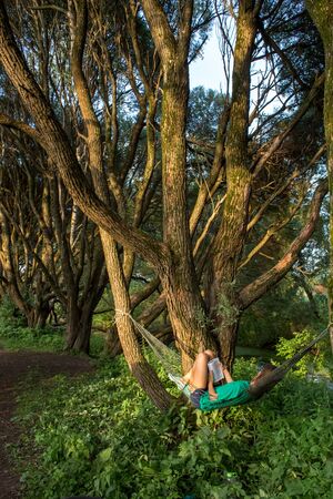 Moscow, Russia - July 21, 2018: The girl reads the book in the city Izmailovo park on a shadow of old curly willowsのeditorial素材