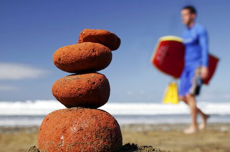 Surfer walking past stone stack on the beach