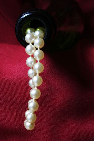 Luxury concept with pearls flowing out of a champagne bottle against a red drapeの写真素材
