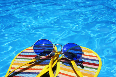 Flip flops and sunglasses by bright blue pool waterの写真素材