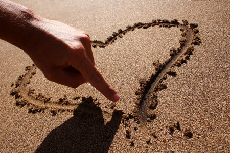 Backlit hand drawing heart in sand on the beachの写真素材