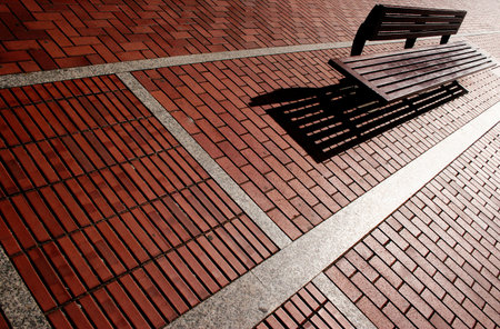 Bench on red brick path with long shadowsの写真素材