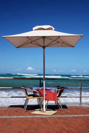 Beachfront table with white umbrella and blue skyの写真素材