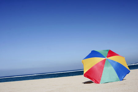Empty beach with single rainbow colored parasolの写真素材