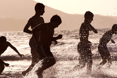 Group of boys running through shallow water at sunsetの写真素材