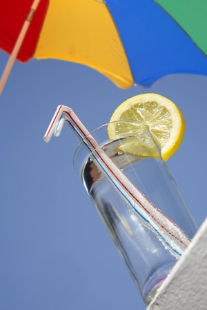 Glass of water on the beach with bright parasolの写真素材